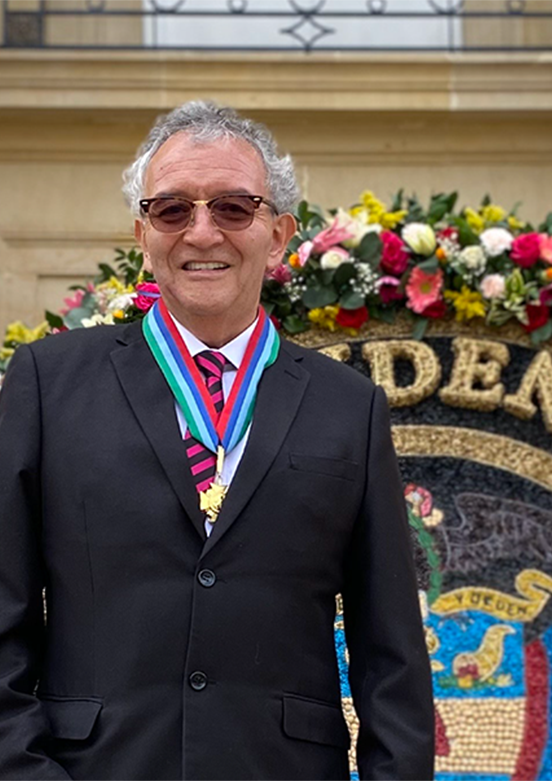 Director de la DNI con medallas frente a un arreglo floral y un escudo de Colombia.